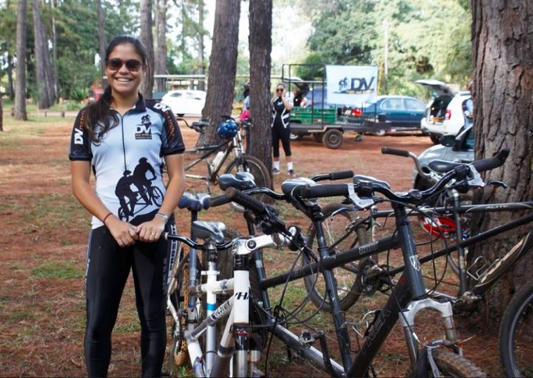 Kimberlly posando pra foto, ao lado de uma tandem, com sorriso de orelha a orelha